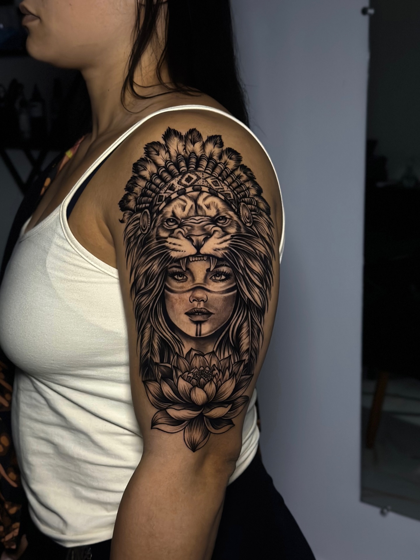 Tatuagem realista de mulher com cocar de leão e flor de lótus no braço
